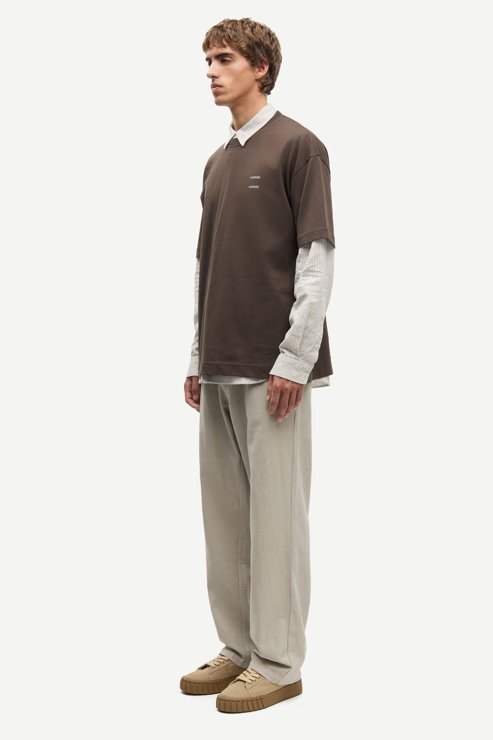 Man wearing a Brown Samsoe Samsoe T shirt over a shirt side view