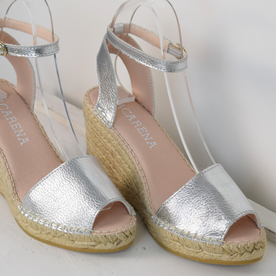 A silver wedge sandal with open toes and an ankle strap 