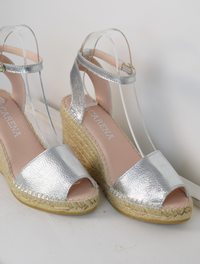 A silver wedge sandal with open toes and an ankle strap 