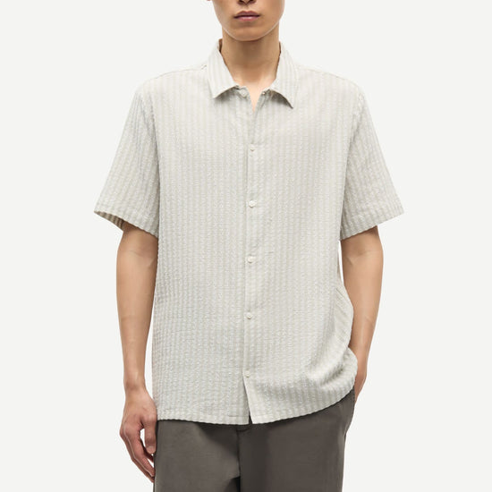 Man wearing a light-colored checkered shirt and gray pants on a white background