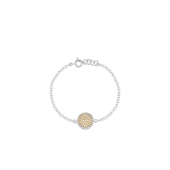 A delicate silver chain bracelet with a central round gold-tone textured disc charm, displayed on a clean white background.