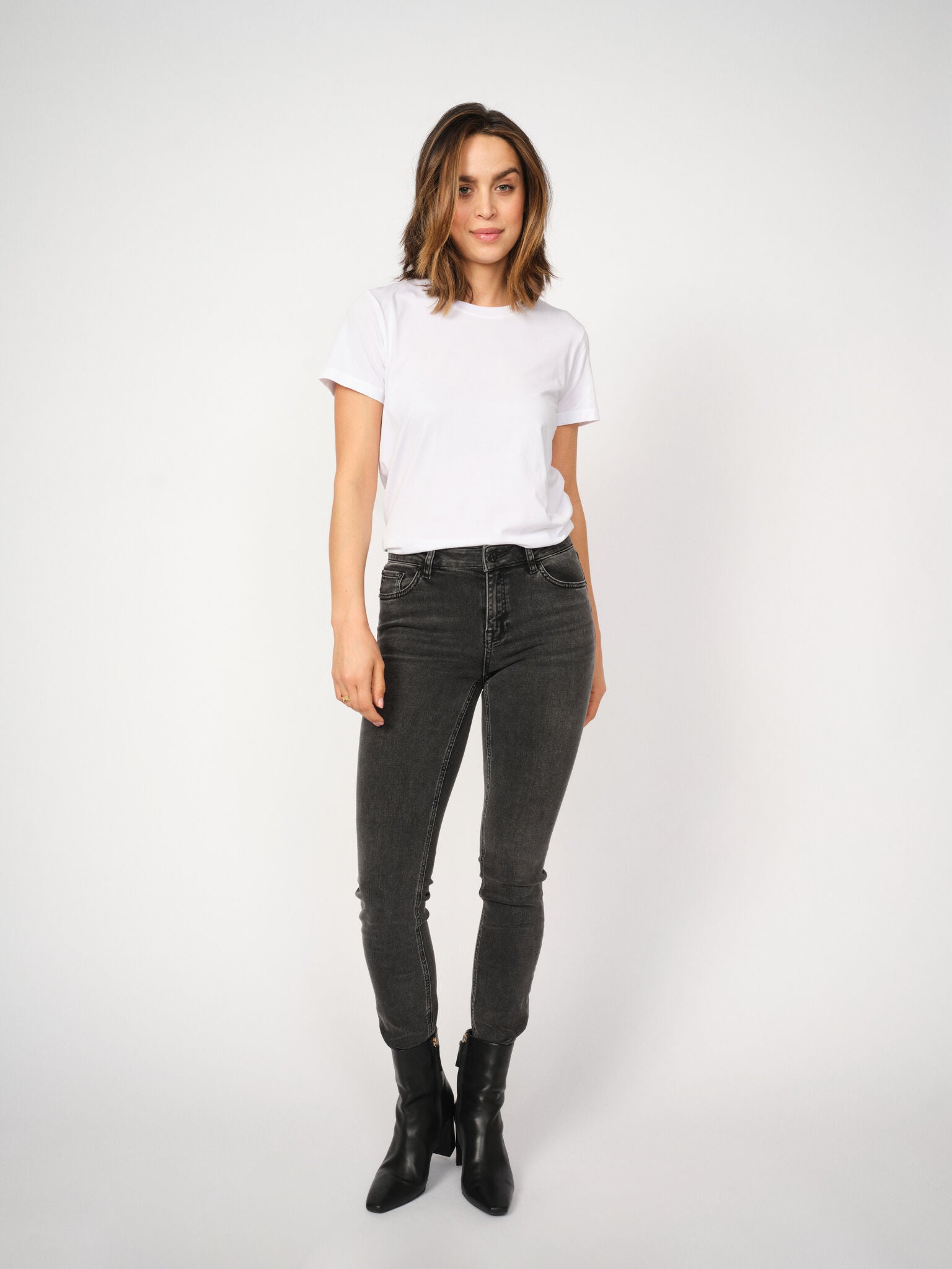 Woman wearing a white t-shirt and grey jeans on a white background