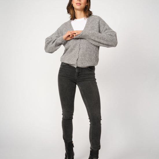 Woman wearing a gray sweater, white shirt, grey jeans, and black boots on a white background
