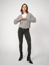 Woman wearing a gray sweater, white shirt, grey jeans, and black boots on a white background