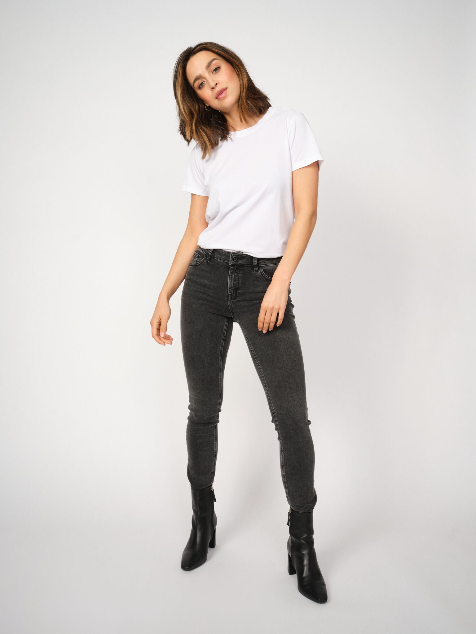 Woman wearing a white t-shirt and grey jeans on a white background
