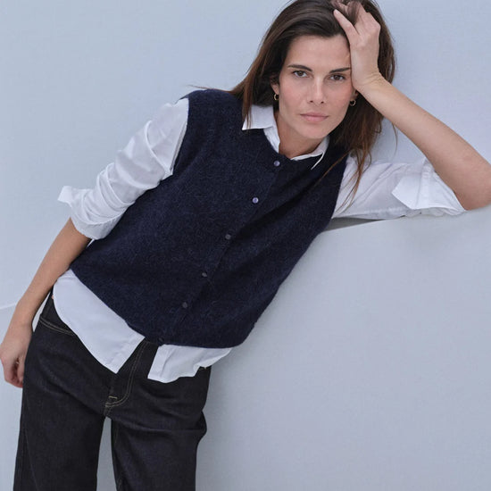 woman wearing a blue knit vest over a white shirt and jeans 