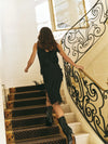 A model photographed walking up stairs in a black skirt and cami outfiit with fringe detailing