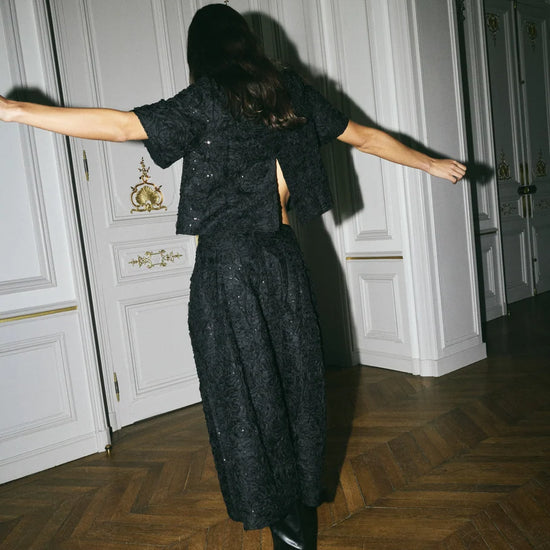 Model shown spinning around wearing a matching black sequins skirt and top set.