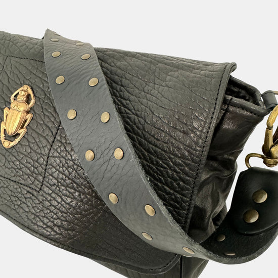 black lamb leather fold over bag with rivet strap and gold scarab emblum close up