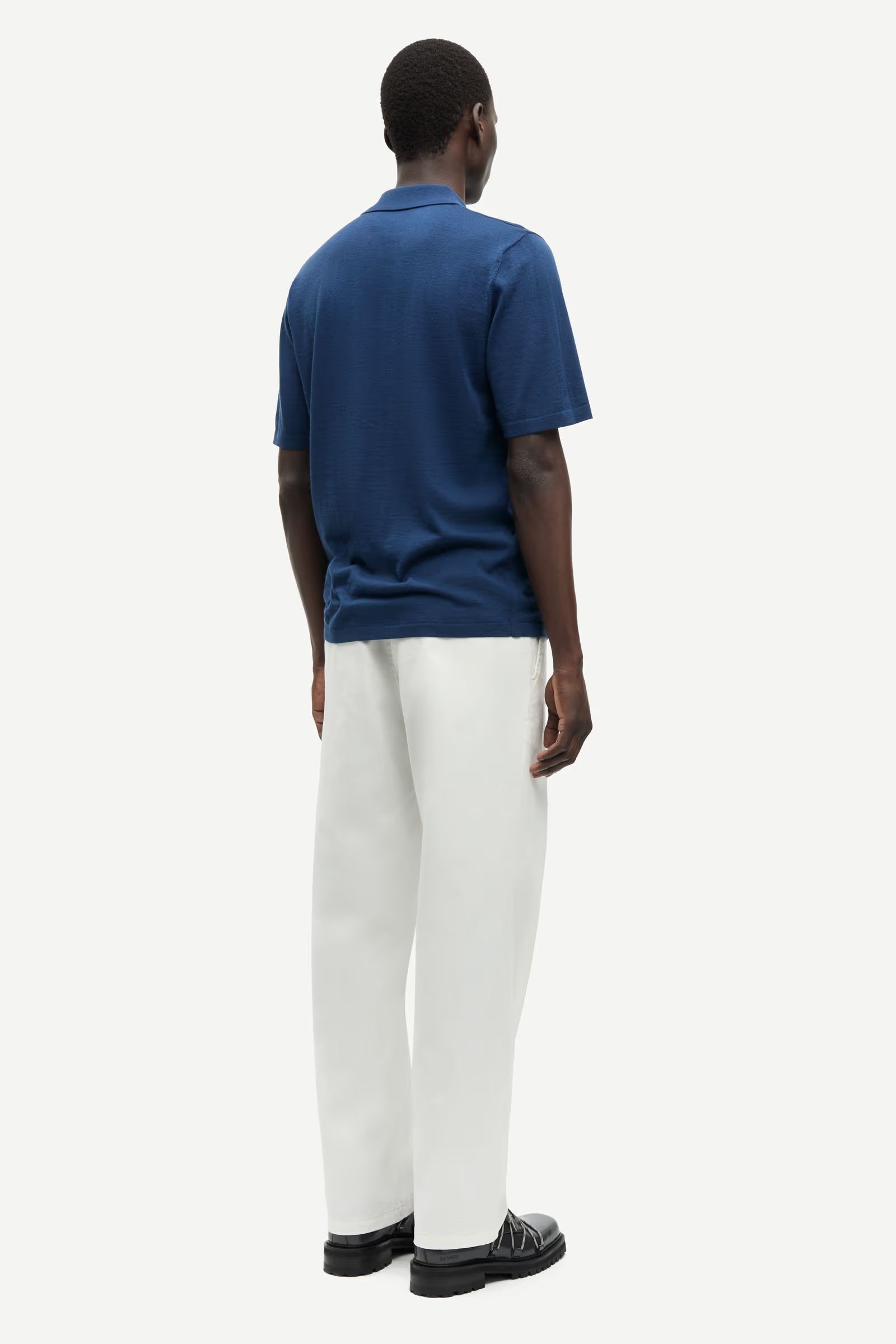 Person wearing a blue polo shirt and white pants on a white background