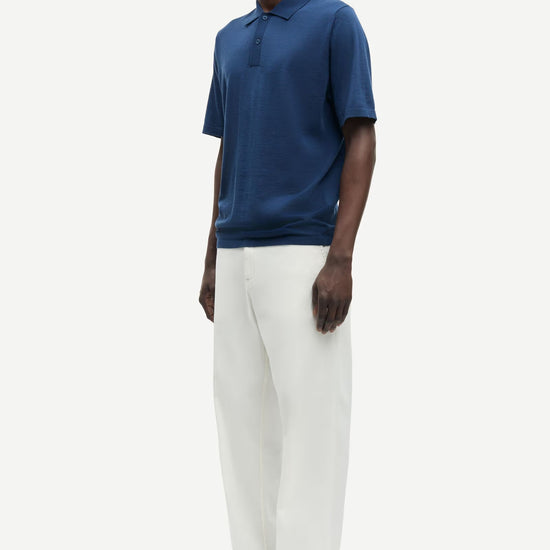 Man wearing a blue polo shirt and white pants on a white background