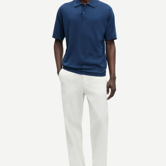 Man wearing a blue polo shirt and white pants on a white background