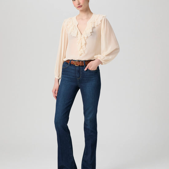 Woman wearing a beige blouse and dark blue jeans on a plain background from Paige