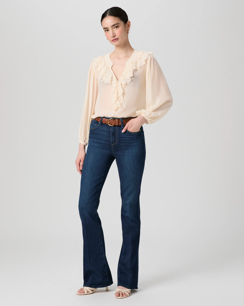 Woman wearing a beige blouse and dark blue jeans on a plain background from Paige