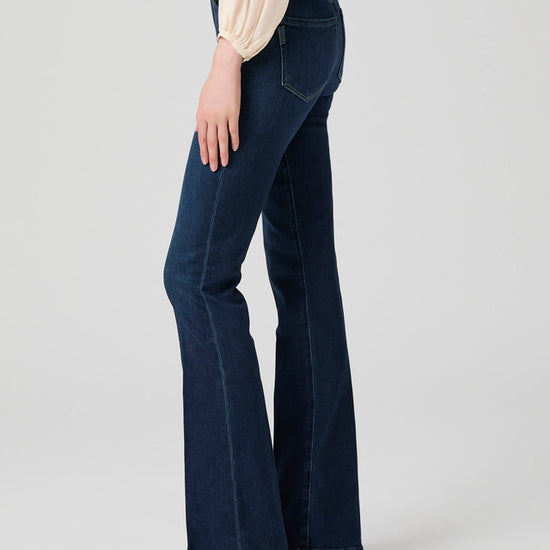 Person wearing dark blue flared jeans on a light gray background