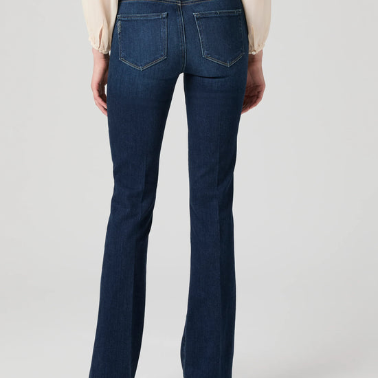 Dark blue jeans worn by a person on a light gray background from Paige