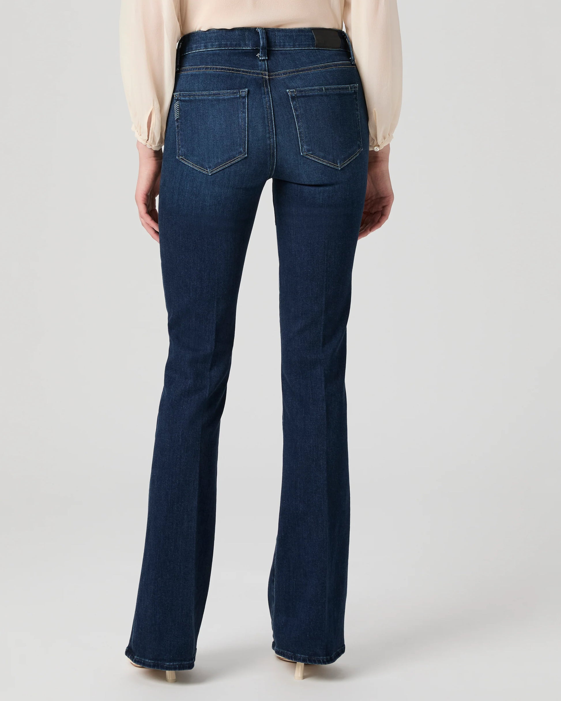Dark blue jeans worn by a person on a light gray background from Paige
