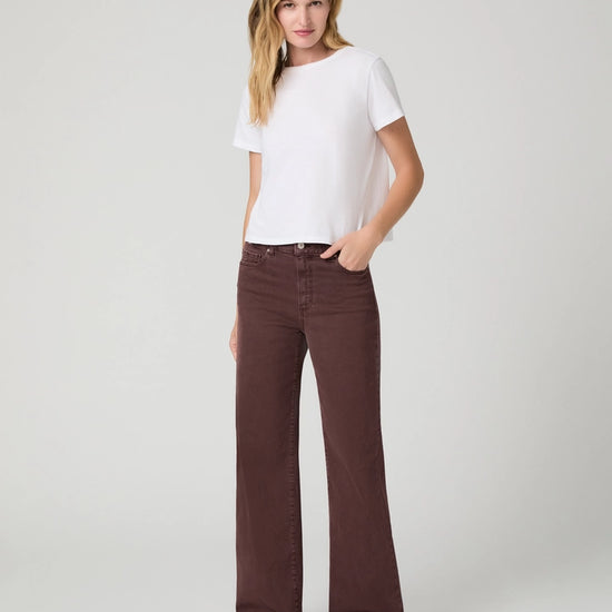 A woman modeling a white short-sleeve crewneck t-shirt and dark brown wide-leg jeans against a light gray studio background.