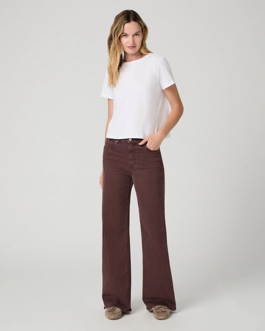A woman modeling a white short-sleeve crewneck t-shirt and dark brown wide-leg jeans against a light gray studio background.