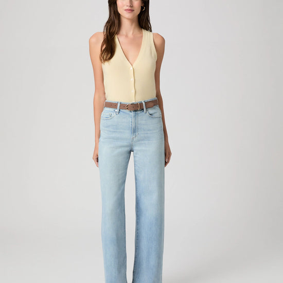 Woman wearing a yellow sleeveless top and light blue jeans on a white background