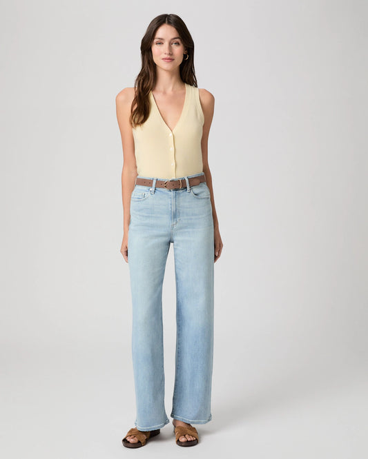 Woman wearing a yellow sleeveless top and light blue jeans on a white background