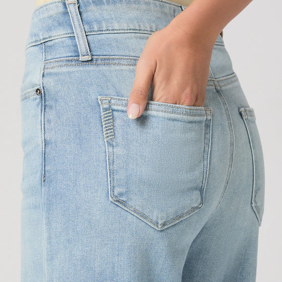 Light blue jeans with a hand in the pocket on a plain background