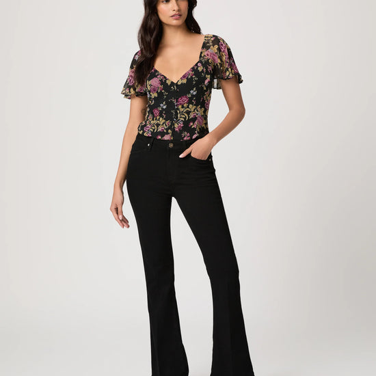 Woman wearing a floral top and black bootleg jeans on a white background