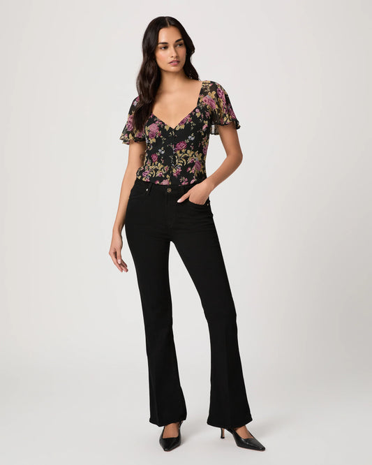 Woman wearing a floral top and black bootleg jeans on a white background