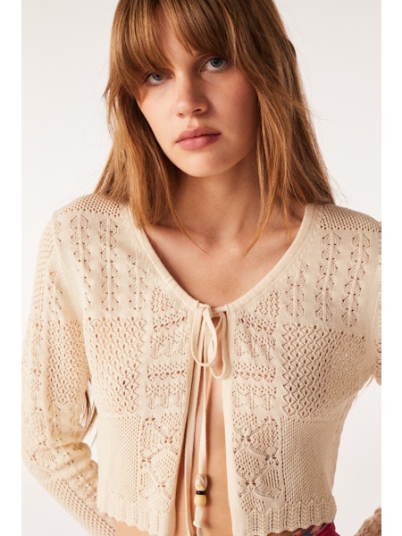 Short fine knit ecru cardigan with crew neck and tie fastening with long sleeves and scalloped edges