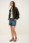 Woman wearing a black leather jacket, white t-shirt, blue denim shorts, and strappy sandals on a white background