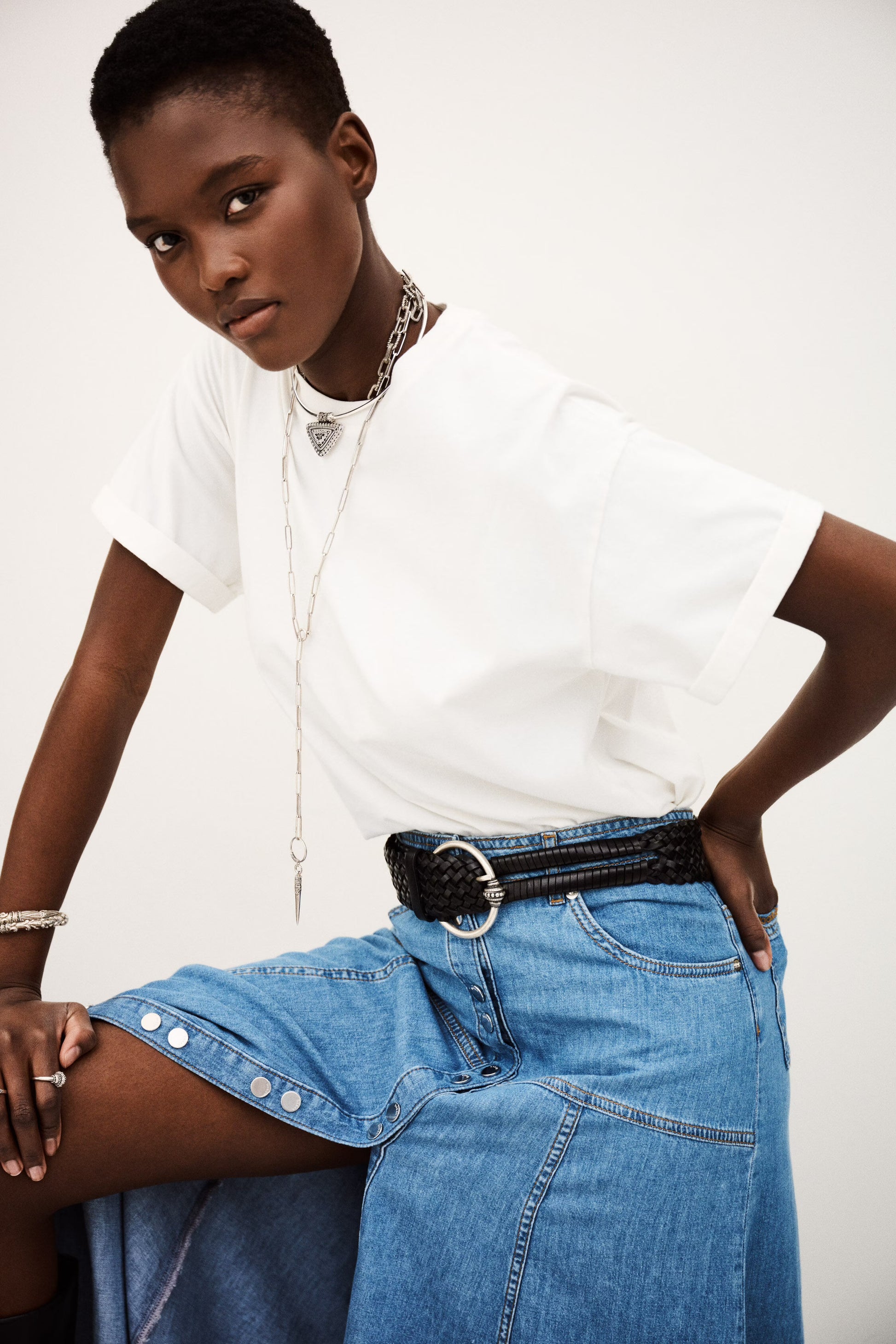 Person wearing a white t-shirt and blue jeans with a belt on a plain background from ba&sh