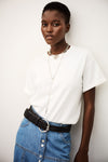 Woman wearing a white t-shirt and blue denim skirt with a black belt against a white background from ba&sh