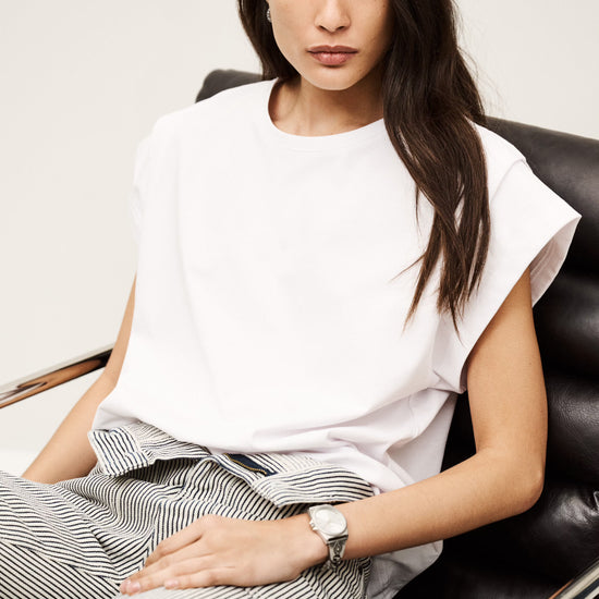 Woman sitting on a black leather chair wearing a white top and striped pants. from ba&sh