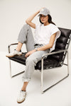 Person sitting on a black chair wearing a white t-shirt, gray pants, and a cap. from ba&sh