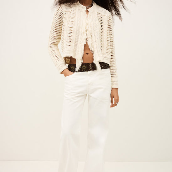 Woman wearing a white knit cardigan and white pants on a plain from background from bash