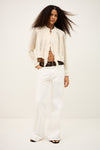 Woman wearing a white knit cardigan and white pants on a plain from background from bash