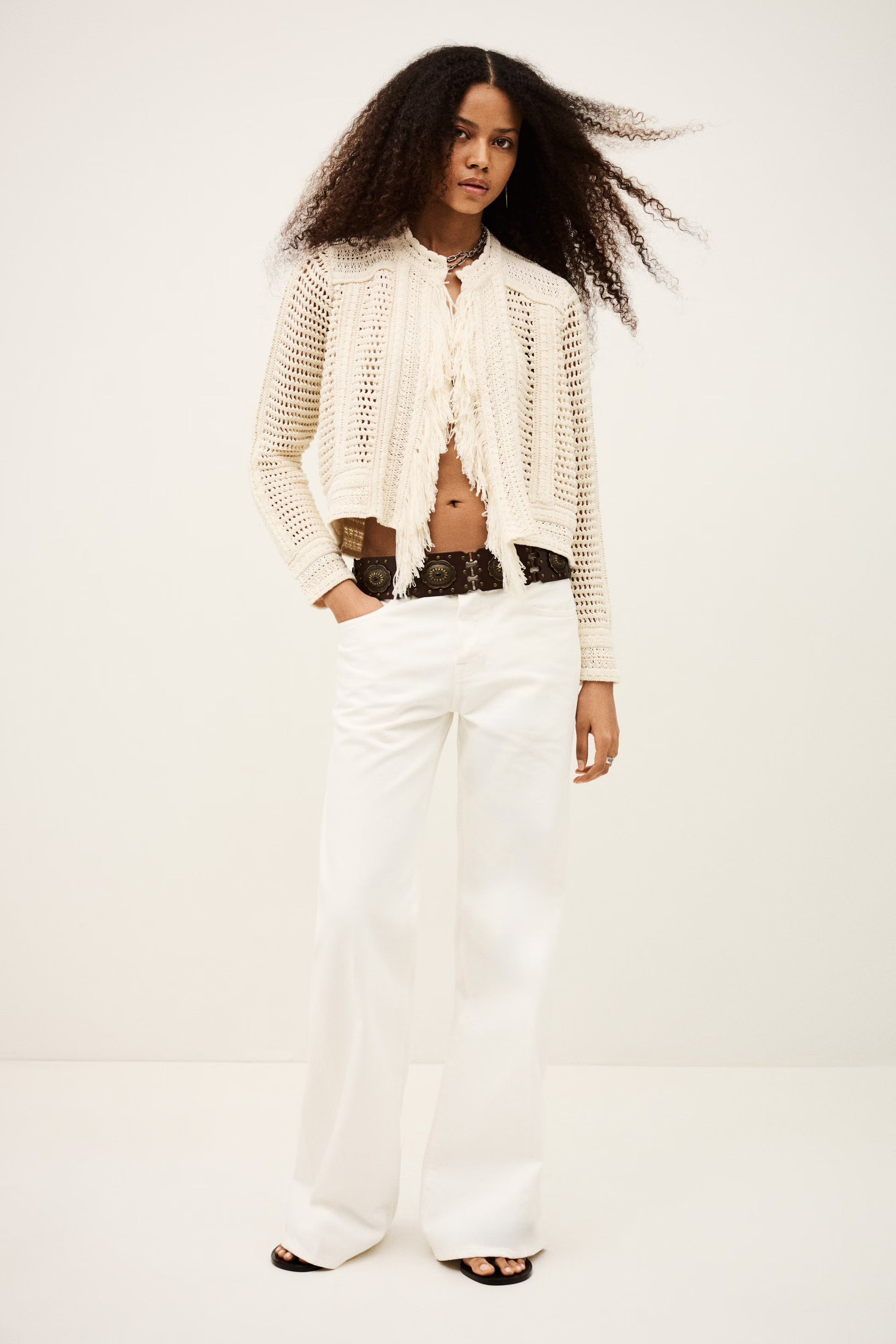 Woman wearing a white knit cardigan and white pants on a plain from background from bash