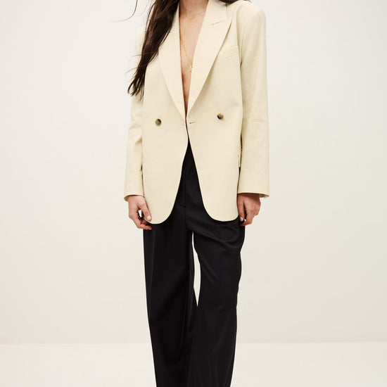 Woman wearing a cream blazer over a black top on a white background from ba&sh