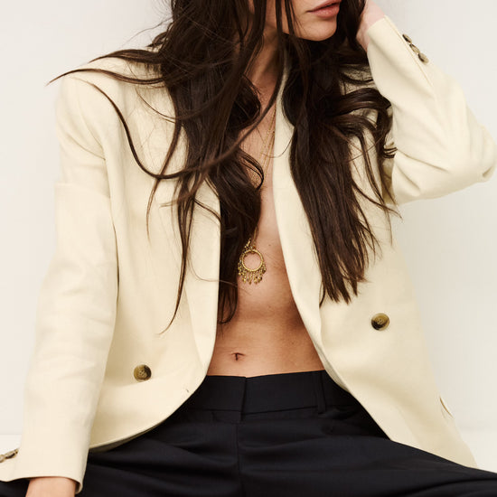 Woman wearing a cream blazer and black pants with a plain background from ba&sh