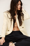 Woman wearing a cream blazer and black pants with a plain background from ba&sh