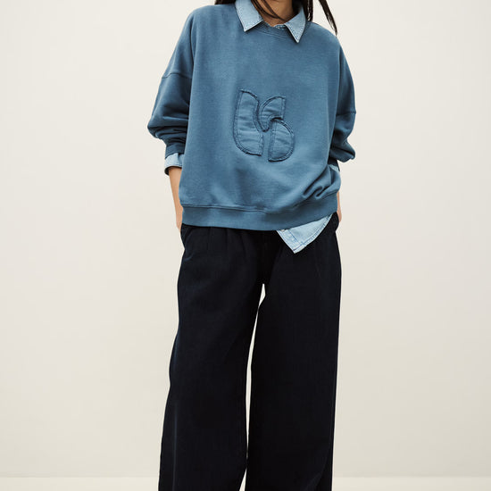 Person wearing a blue sweater and black pants on a white background