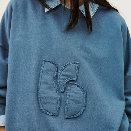 Blue sweatshirt with a unique design on the chest against a neutral background