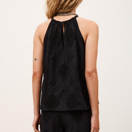 Person wearing a black sleeveless top with floral embroidery on a plain background