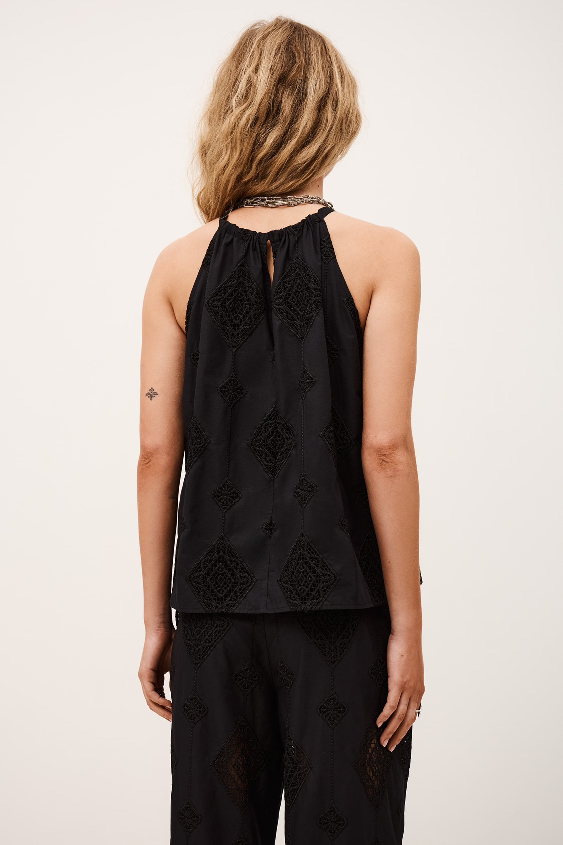 Person wearing a black sleeveless top with floral embroidery on a plain background