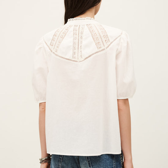 Person wearing a white blouse with lace details and blue jeans on a plain background
