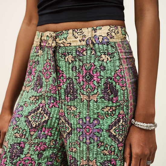 Person wearing a black top and green patterned pants on a plain background