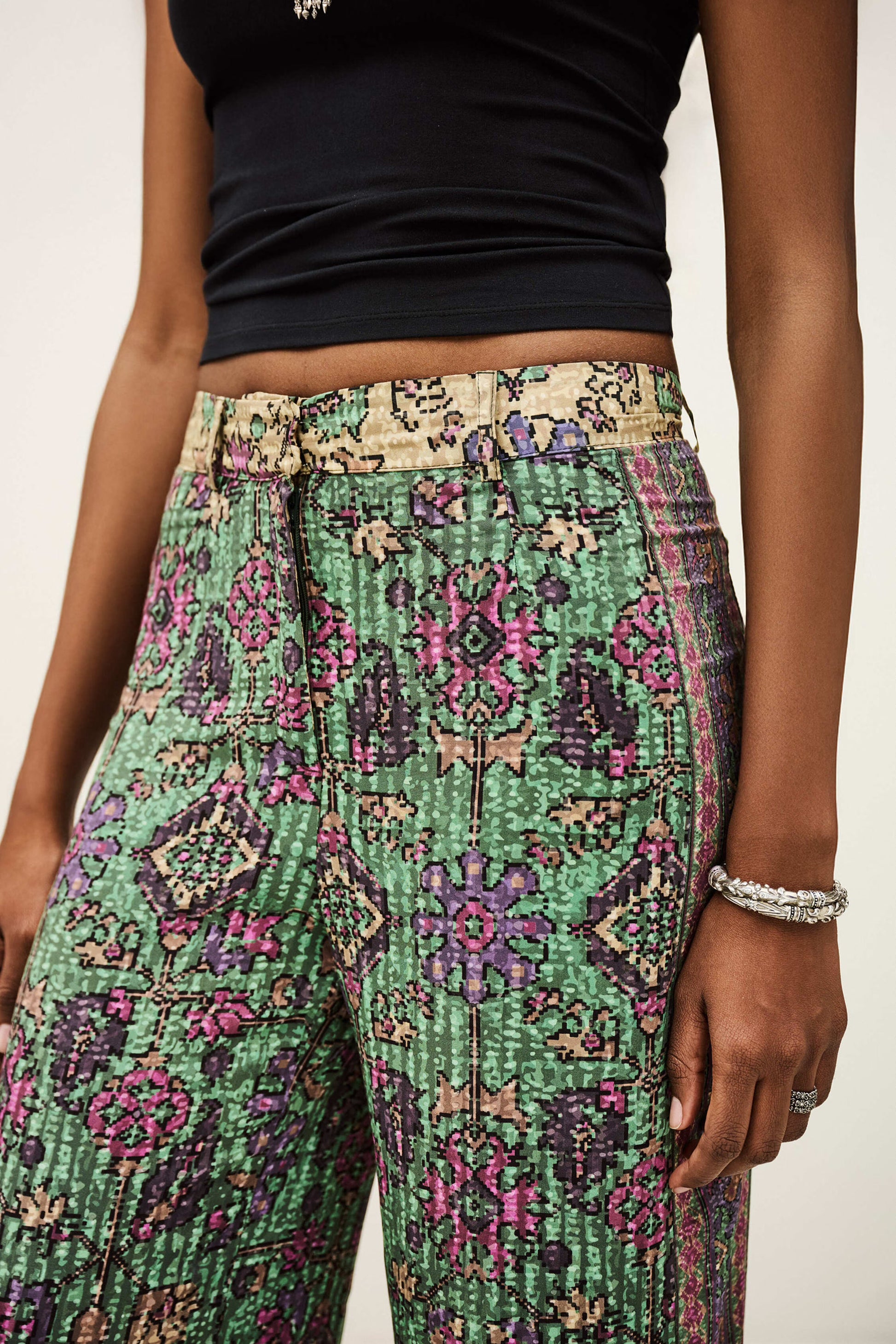 Person wearing a black top and green patterned pants on a plain background