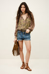 Woman wearing a patterned blouse, denim shorts, and brown sandals with a white background