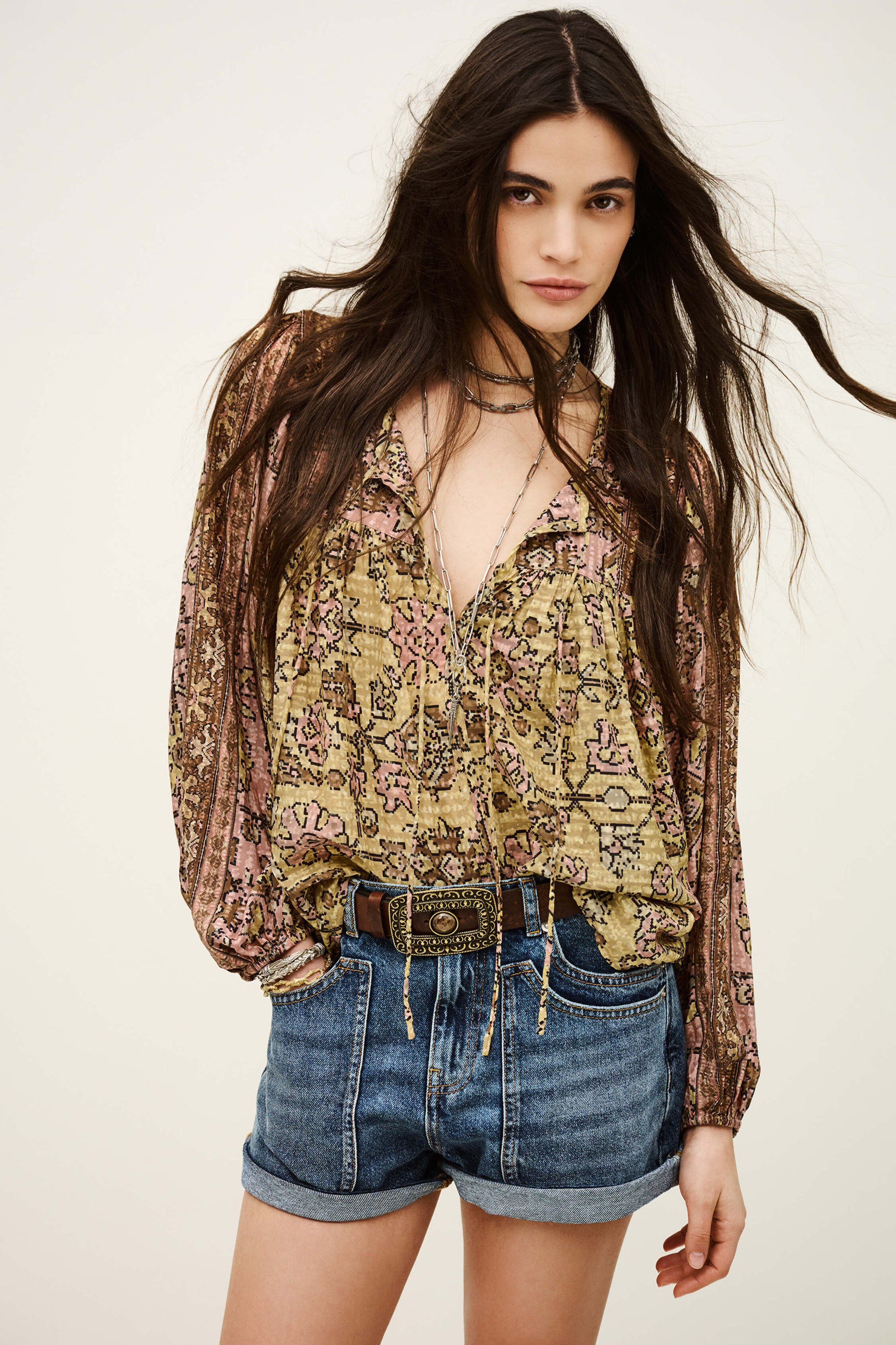 Woman wearing a floral blouse and denim shorts on a plain background