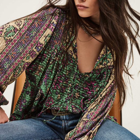 Woman wearing a patterned blouse and jeans sitting on a chair.